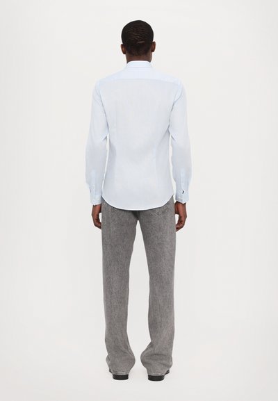 Cămașă lungă cu mâneci lungi de culoare albastru deschis, cu un guler ascuțit și manșete cu nasturi, asortată cu pantaloni gri cu picioare largi. Design simplu și croit.
