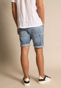 Pantalones cortos de mezclilla en azul claro, con dobladillo enrollado, dos bolsillos traseros con costuras decorativas, combinados con una camiseta blanca y zapatillas negras.