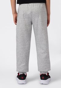 Pantalones deportivos grises con cintura elástica, puños ajustados y bolsillos, combinados con zapatillas deportivas negras con acentos rojos.