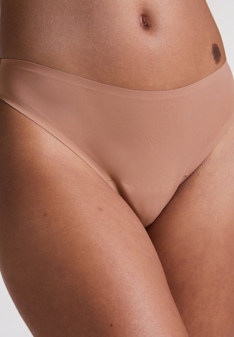 De taille van een vrouw in naadloze huidkleurige ondergoed, toont huidtextuur, navel en een donkere moedervlek aan de rechterzijde.