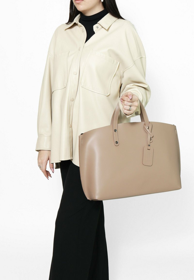 Beige lederen handtas met een gestructureerde vorm, dubbele handvatten en een bagagelabel detail. Gladde textuur met contrasterende stiksels.