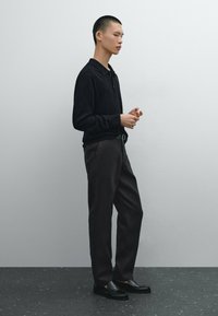 Black knit polo shirt, dark grey trousers, and black loafers. The outfit features a slim fit and minimalistic design with subtle textures.