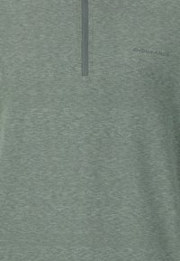 Kortærmet, lynlås-pullover i meleret lys grøn stof. Har en glat tekstur og et lille logo-detail på fronten.