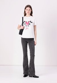 White cotton t-shirt with graphic design featuring pink heart and characters, paired with black flared jeans and black ankle boots.