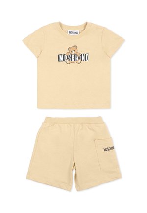 Set per bambino piccolo beige composto da t-shirt e pantaloncini con grafica di un orsetto e scritta "MOSCHINO" sulla maglietta e sulla tasca.