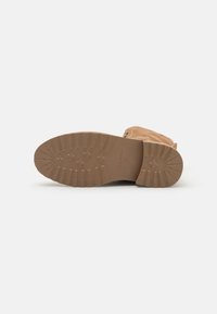Bota de ante marrón con punta redondeada, que presenta una suela de goma texturizada y un tacón bajo. Marca estampada cerca de la zona del talón.