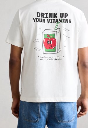 Hvid t-shirt med tegneserie juiceboks med et rødt æble og grønstribet sugerør, tekst "Drink up your vitamins" på bagsiden.