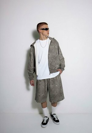 Szary zestaw z nadrukiem w postaci bluzy z kapturem i szortów z wzorem paisley, połączony z białą koszulką i czarnymi sneakersami. Uzupełniony okularkami przeciwsłonecznymi.