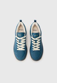 Teal syntetiske joggesko med perforert tåboks, beige snøringer og logo på tungen. Rundt tåparti og polstret krage med kontrasterende såle.