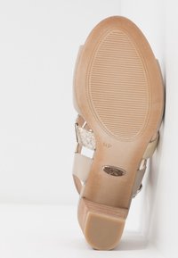 Sandale à talons beige avec une tige texturée, présentant une fine sangle métallique décorative et une semelle en caoutchouc striée pour une meilleure adhérence et stabilité.