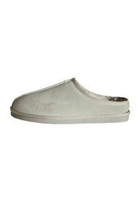 Chausson en daim gris clair avec un dos ouvert, un bout arrondi et un intérieur doux. Présente des coutures visibles le long des bords et une semelle plate.