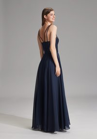 Abito da sera blu navy con un corpetto decorato di perline, spalline sottili e una gonna fluente fino alla caviglia. Tessuto liscio, design elegante e vita aderente.