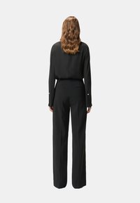 Blusa nera a maniche lunghe con una texture liscia e polsini con bottoni, abbinata a pantaloni neri a vita alta e gamba larga con una tasca posteriore.