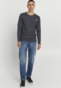 Langarm-Graues T-Shirt mit rundem Halsausschnitt und kleinem Logo, kombiniert mit hellblauen Jeans und schwarzen Sneakers. Einfaches und lässiges Design.