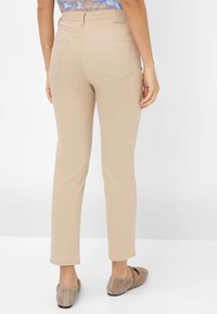 Beige, slim-fit broeken met een gladde textuur en nette naden. Voorzien van twee achterzakken en een middelhoge taille. Gepaard met grijze instappers.