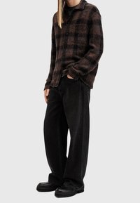 Brun och svart rutig flanellskjorta, knäppt, med bröstficka, i kombination med vida svarta jeans och kraftiga svarta stövlar.