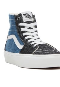 Baskets montantes en denim bleu et noir, avec des lacets blancs, un col rembourré et une étiquette de marque sur la languette.