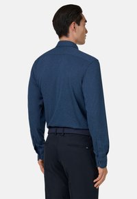 Langarmshirt in een donkerblauwe, gestructureerde stof met een spread collar. Het heeft knoopmanchetten en wordt gedragen met een marineblauwe broek.