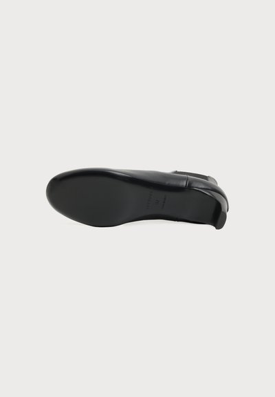 Chaussure habillée en cuir noir vue de la semelle avec un petit talon sur un fond clair uni.