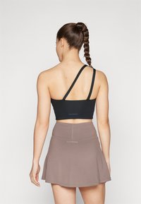 Top corto negro con un tirante, combinado con una falda acampanada de color marrón claro. Tela suave, diseño minimalista y logo de la marca visible en la banda.