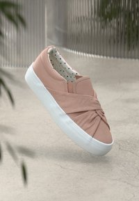 Rozā slip-on apavi ar mezglu dizainu, auduma materiāls, balta gumijas zole un punktiņainas oderes. Kopumā gluda tekstūra.