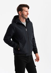 Marinblå hooded jacka i mjukt tyg, med dragkedja fram, sidofickor, ribbade ärmslut och nederkant, tillsammans med svarta cargobyxor.