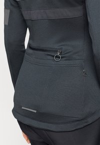Musträne must sportjakker, mille struktuurse kanga, horisontaalsete hallide triipudega, lukuga tagatasku ja ümmargune luku tõmbamine detail.