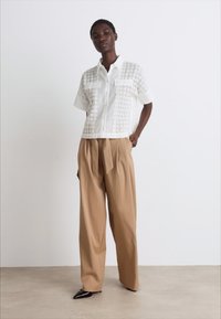 White shirt with textured embroidered design, two chest pockets, paired with loose beige trousers and black pointed shoes.
