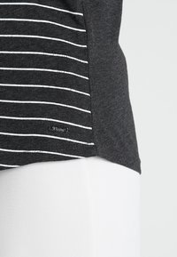 Mörkgrå t-shirt med vita horisontella ränder och en liten metall-logotyp. Mjuk tygkvalitet med avslappnad passform och rundad nederkant.