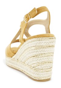 Wedge sandal featuring a tan suede upper and a braided jute heel with gold thread accents. Open heel design with adjustable strap.