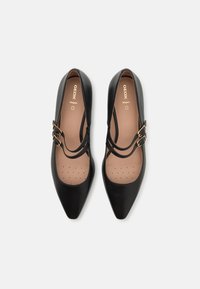 Chaussures Mary Jane noires pour femmes à bout pointu, double bride et boucles dorées, semelles intérieures beiges perforées pour la respirabilité.
