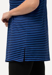 Pruhovaná tunika s modrými a tmavě námořnickými vodorovnými pruhy, se bočním rozparkem a měkkou tkaninou. Zkombinována s černými legínami na dolní části.