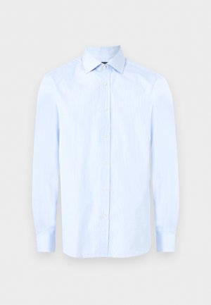 Chemise habillée homme bleu clair à manches longues avec col pointu et boutons blancs sur le devant, sur un fond uni.