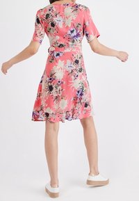 Robe à fleurs à manches courtes rose, avec des fleurs violettes et blanches, une taille cintrée et une jupe évasée ; associée à des baskets blanches.