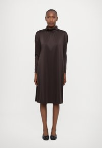 Abito lungo marrone con maniche lunghe e collo alto, caratterizzato da una vestibilità comoda e una texture liscia, che arriva poco sopra il ginocchio.