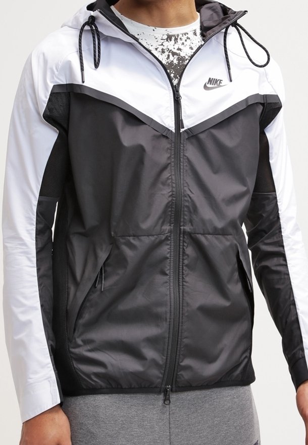 Svart och vit vindtät jacka med dragkedja fram, snörning i huvan, sidofickor och Nike-logotyp på bröstet; har en färgblockdesign.