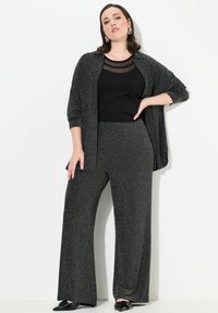 Ensemble en deux pièces comprenant un haut noir avec des accents en maille, un châle texturé assorti et un pantalon large en niveaux de gris. Des chaussures plates noires sont incluses.