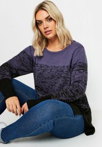 Maglione lavorato a maglia viola e nero con un design testurizzato, polsini a coste e scollatura rotonda, abbinato a jeans blu.
