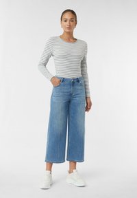 Gestreiftes Langarmhemd in Grau und Weiß, kombiniert mit hellblauen weit geschnittenen Jeans. Das Modell trägt weiße Sneakers. Schlichte, lässige Kleidung.