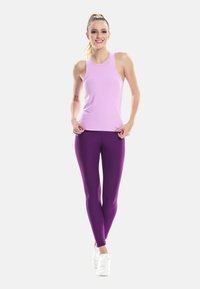 Fioletowe legginsy zestawione z jasnoróżowym topem na ramiączkach. Dopasowany top ma cienkie ramiączka, a legginsy mają gładką, elastyczną strukturę. Białe sneakersy.