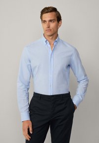 Lichtblauw overhemd met lange mouwen, voorzien van een subtiele textuur, button-down kraag en een klein geborduurd logo op de borst.