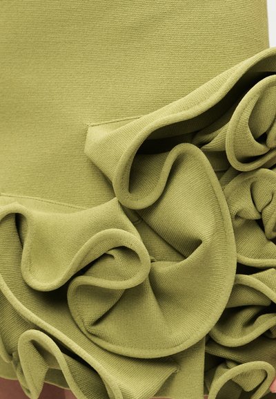 Κοντινή λήψη πράσινου υφάσματος με παχιά, δομημένα βολάν που δημιουργούν στρωματοποιημένη, κυματιστή υφή και πτυχές.