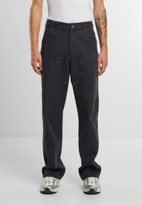 Pantalones negros de corte relajado, con grandes bolsillos frontales, detalles en dorado y una tela suave y texturizada.