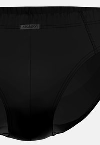 Slip da bagno neri con cuciture visibili e un piccolo etichetta rettangolare con la scritta "AMMANN" sulla cintura anteriore.