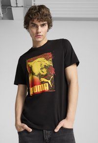 Camiseta de algodón negra con un gráfico de la cabeza de un león en amarillo y rojo, con el texto y el logo de "PUMA". Diseño de manga corta y cuello redondo.