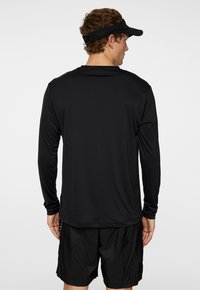 Svart långärmad träningsskjorta med en slät yta, med rundad halsringning och något figursydd design, matchad med svarta shorts.