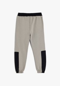 Grå joggerbyxor med svarta detaljer, elastisk midja och avsmalnande muddar; tillverkade av mjukt material med en slät textur.