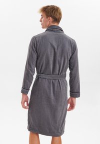 Accappatoio da uomo grigio realizzato in morbido tessuto peloso. Presenta un colletto a scialle, maniche lunghe e una cintura in vita. Texture liscia in tutto il capo.