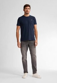 Mörkblå t-shirt med rund hals och korta ärmar, med en liten logga på bröstet, kombinerad med blekta grå jeans och vita sneakers.