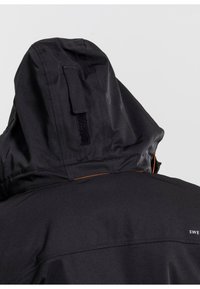 Giacca impermeabile nera con cappuccio, caratterizzata da una superficie testurizzata e un accento arancione nella fodera interna. Chiusura in velcro sul retro del cappuccio.